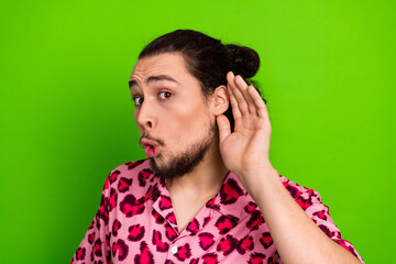 Young man posing with a hand-to-ear gesture in a pink leopard print shirt on a vibrant green...
