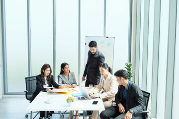 Corporate professionals discussing project strategy at meeting table with charts on whiteboard, representing innovation, collaboration, and teamwork in workplace.