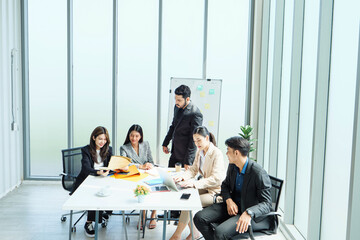 Southeast Asian business professionals in formal attire gathered in modern office, leader...