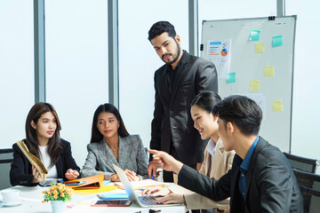 Group of Southeast Asian executives sitting around table in bright office, leader pointing at chart with confidence, representing collaboration, strategic planning, and leadership in business.