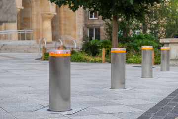 A row of modern retractable security bollards with red indicator lights standing on a paved urban...