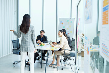 Group of professionals sitting around meeting table listening to female leader presenting ideas,...