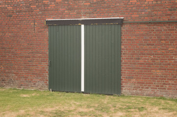 Green sliding barn doors closing a brick wall opening in a farm