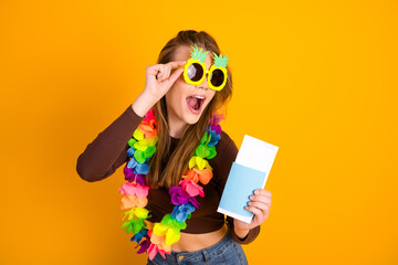 Excited young woman with colorful tropical accessories holding a ticket against a vibrant yellow...