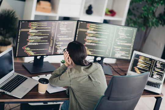 Young female programmer working at a desk with multiple computers coding software in a modern home office