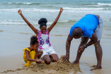 Joyful family enjoys sunny day at beach, with children playing in sand while adult builds...