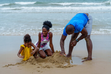Joyful family enjoys sunny day at beach, building sandcastles together. Laughter fills air as they...