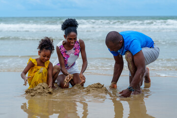Joyful family enjoys sunny day at beach, building sandcastles together while waves gently lap at...