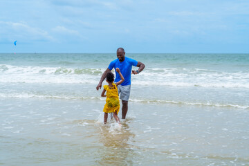 Joyful family enjoys sunny day at beach, where father plays with his child in gentle waves,...