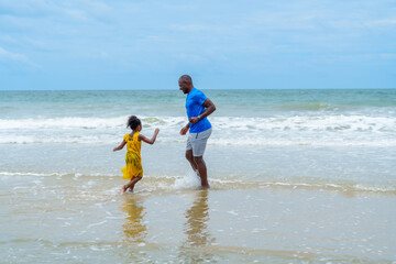 Joyful family enjoys sunny day at beach, where father and daughter play together in gentle waves,...