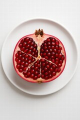Fresh pomegranate cut in half showing red juicy seeds served on white plate top view