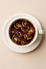 White cup filled with iced black coffee and ice cubes served on light background top view