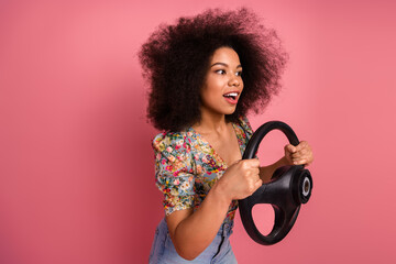 Beautiful young woman holding a steering wheel with cheerful expression against a vibrant pink...