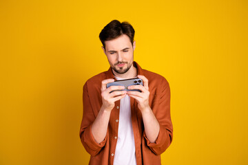 Handsome man in casual attire engrossed with a smartphone against a vibrant yellow background...