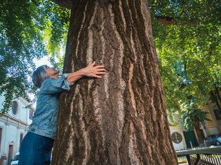 A person embracing the trunk of a large majestic tree in a park setting during springtime sunlight highlighting the textured bark and green foliage