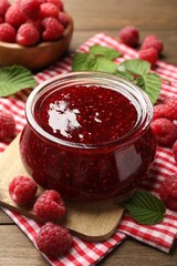 Tasty jam, fresh ripe raspberries and leaves on wooden table, closeup.