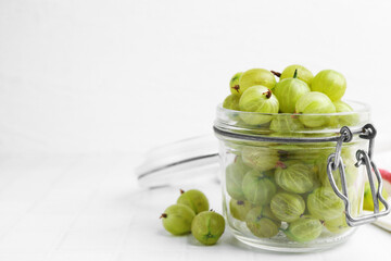 Fresh green gooseberries in jar on white table, closeup. Space for text