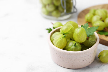 Fresh green gooseberries in bowl on white table, closeup. Space for text
