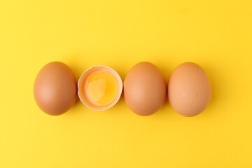 Whole and broken chicken eggs on yellow background, top view