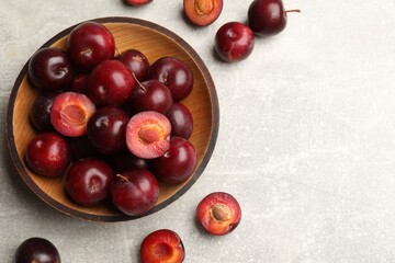Ripe cherry plums and bowl on grey textured table, flat lay. Space for text