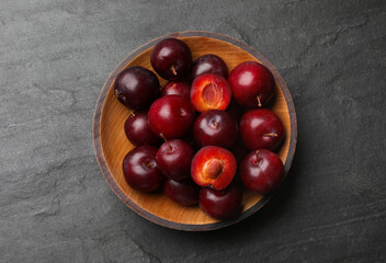 Ripe cherry plums in bowl on dark textured table, top view