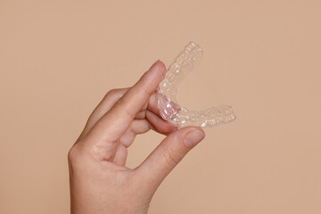 Woman with dental aligner on beige background, closeup