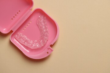 Clear aligner in retainer case on beige background, top view. Space for text