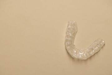 One clear aligner on beige background, top view. Space for text