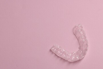 One clear aligner on pink background, top view. Space for text