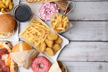 Different delicious fast food and cola on light wooden table, flat lay. Space for text