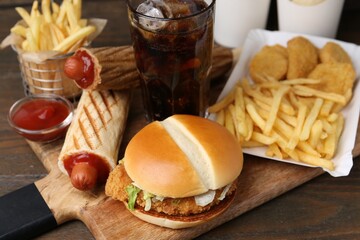 Different delicious fast food and cola on wooden table, closeup