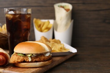 Delicious burger, cola and other fast food on wooden table, closeup. Space for text