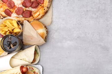 Different delicious fast food and cola on light grey textured table, flat lay. Space for text