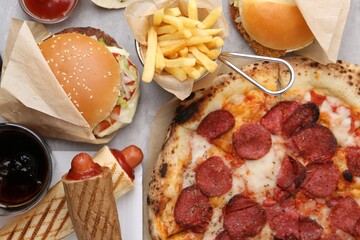 Different delicious fast food and cola on light grey table, flat lay