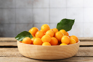 Ripe yellow cherry plums and leaves on wooden table, closeup