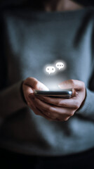 Close-up of a person's hands holding a smartphone with illuminated chat bubbles hovering over the display