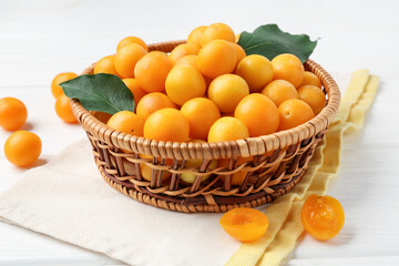 Ripe yellow cherry plums with leaves on white wooden table, closeup