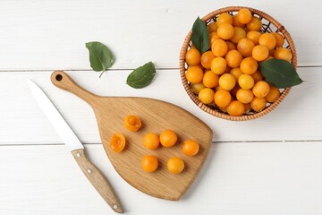 Ripe yellow cherry plums with leaves and knife on white wooden table, flat lay
