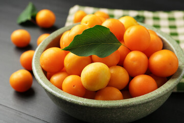 Ripe yellow cherry plums with leaves on black wooden table, closeup
