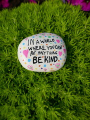 In a world where you can be anything be kind kindness rock on green moss vertical photo