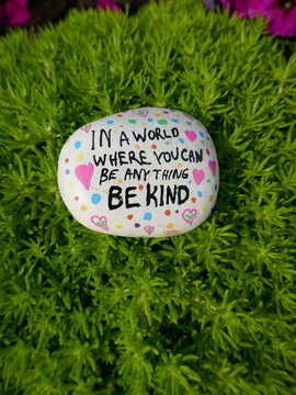 In a world where you can be anything be kind kindness rock on green moss vertical photo