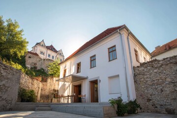 Historic stone building with modern design in a sunlit courtyard surrounded by ancient walls, featuring tables and chairs for outdoor dining in a charming location