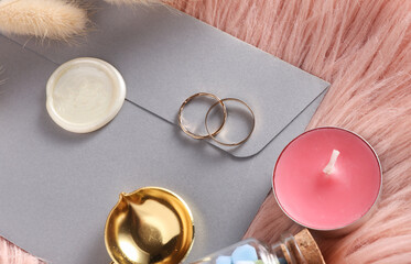 Envelope with wax seal stamp and two gold rings on pink fleecy background. Wedding invitation