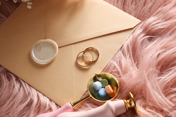 Obraz premium Envelope with wax seal, vintage stamp and two gold rings on pink fuzzy background. Wedding invitation