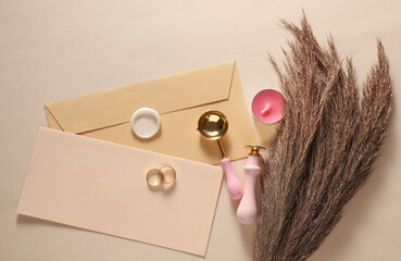 Wedding invitation stationery set. Envelope with sealing wax, vintage stamps and gold rings, dry grass on beige background