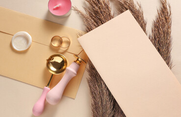 Wedding invitation stationery set. Card, Envelope with sealing wax, vintage stamps and gold rings, dry grass on beige background