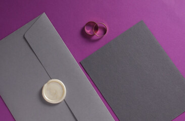 Wedding invitation stationery set. Envelope with sealing wax and gold rings on purple background