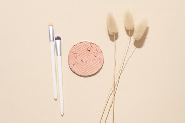 Crushed eyeshadow for makeup with brush and dry grass. Cosmetic product sample on beige background. Minimalism beauty concept. Top view. Flat lay
