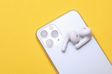Back view of a modern white smartphone with three cameras and wirelass earphones on yellow...
