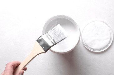 Hand holding brush and Open can of white paint on concrete background. Top view